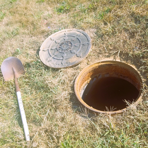 Shovel and manhole lid laying on ground next to an open manhole