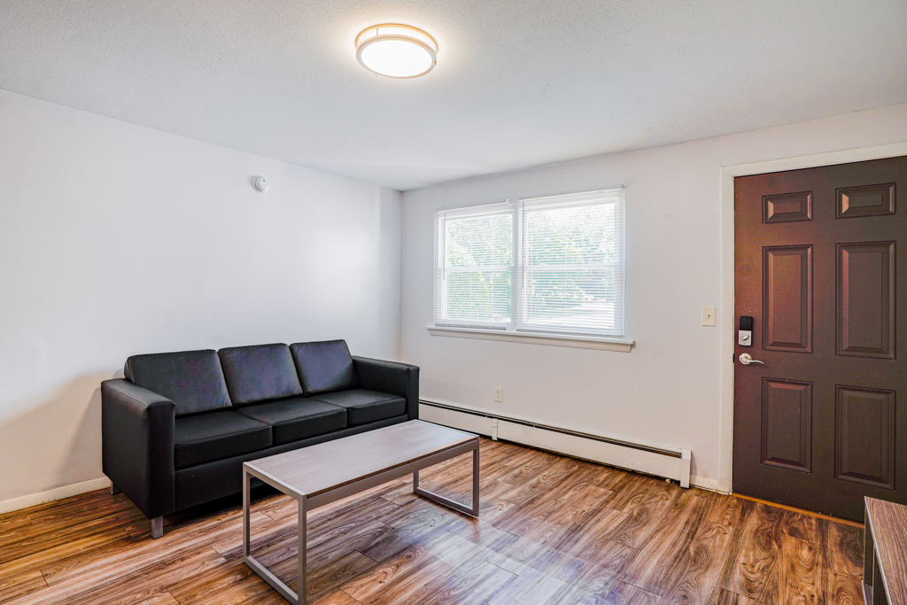 Modern living room at The Den in Willington, CT, featuring a black leather sofa, coffee table, and large window