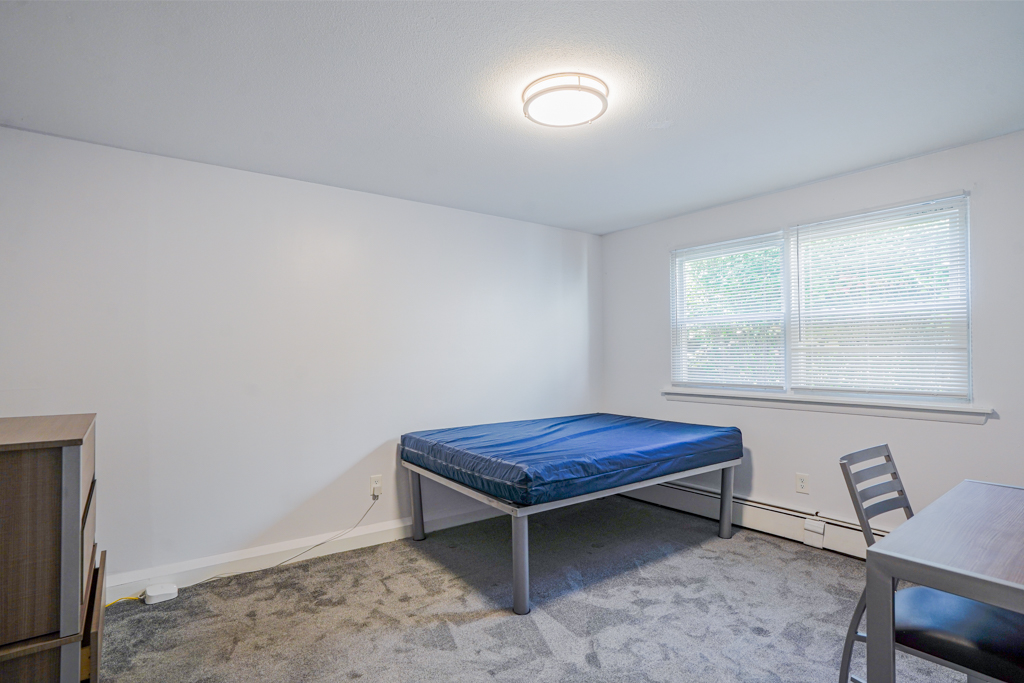 Cozy bedroom at The Den in Willington, CT, styled with a metal bed frame, desk area, wardrobe, and large window