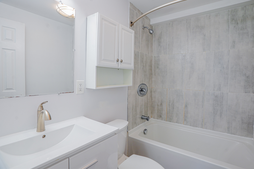 Bathroom at The Den apartments in Willington, CT, showcasing a modern gray vanity, brushed gold hardware, and a bright, clean bathtub and shower enclosure.