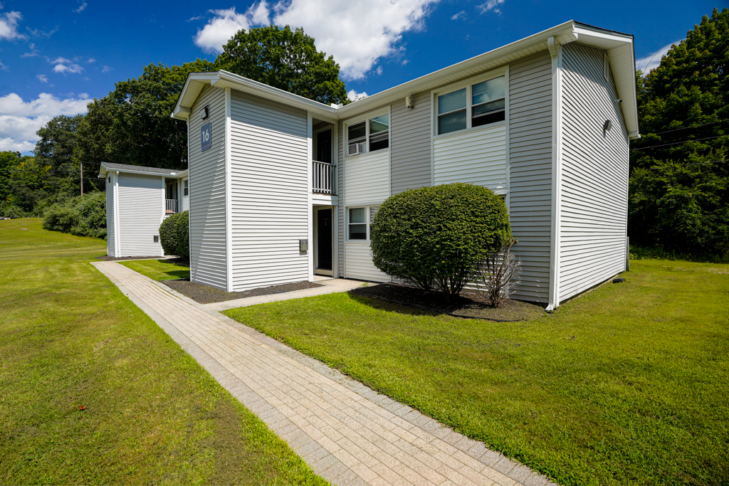 Exterior view of The Den apartment community in Willington, CT, showing residential building surrounded by trees.
