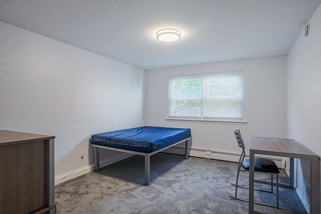 Cozy bedroom at The Den in Willington, CT, styled with a metal bed frame, desk area, and large window