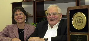Laurie Branch, current CEO of Ironpeak, is sitting with her dad, Paul Branch, and a retirement plaque. 