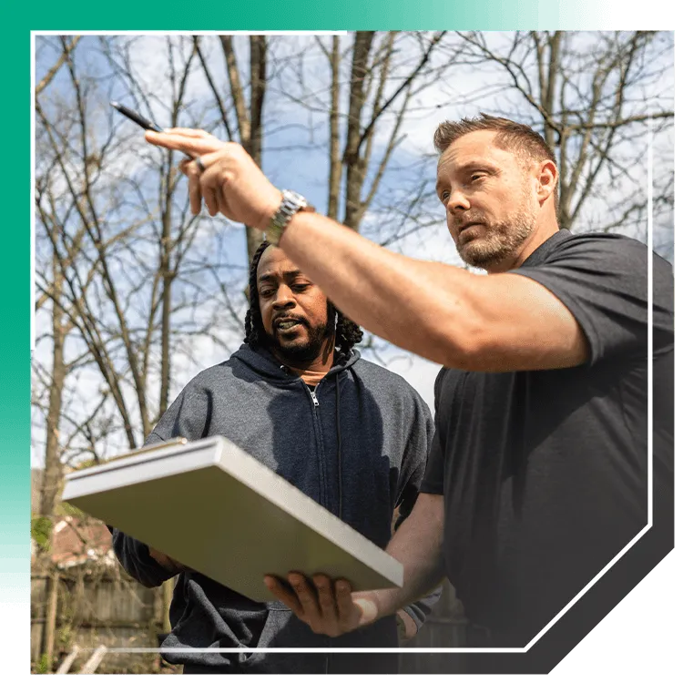 Contractor pointing while reviewing clipboard with homeowner in backyard during a foundation inspection