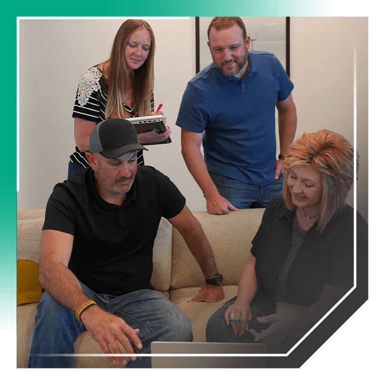 Four people gathered on a couch reviewing a foundation repair estimate on a laptop during an in-home consultation