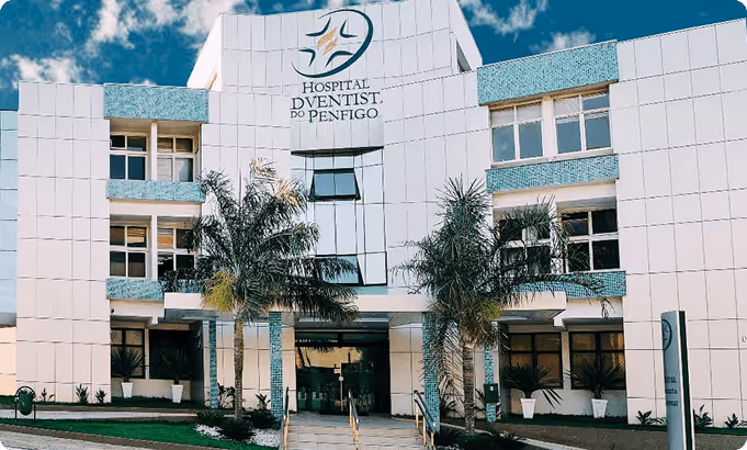 Fachada do Hospital Odontológico do Penfigo com plantas em frente e céu azul ao fundo.