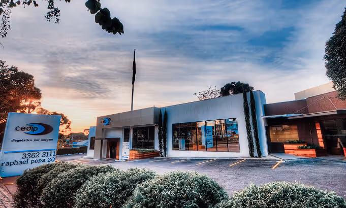 Fachada de clínica de diagnóstico por imagem Cedip com estacionamento vazio e céu ao entardecer.