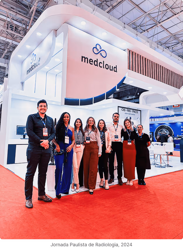 Equipe da Medcloud posando com crachás em um estande branco com luzes em feira de radiologia com tapete vermelho.
