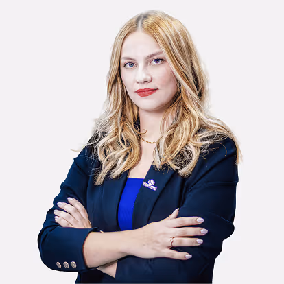 Mulher loira com cabelo ondulado usando blazer azul escuro com braços cruzados, posando confiante.