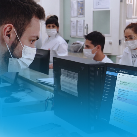 Profissionais de saúde usando máscaras e computadores em ambiente hospitalar.