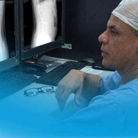 Médico analisando raio-x da coluna vertebral em dois monitores em ambiente clínico.