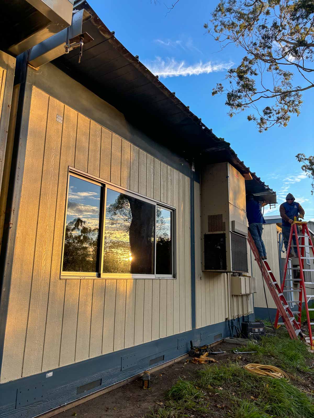 Before: worker on a ladder inspecting the damaged eave of a modular classroom