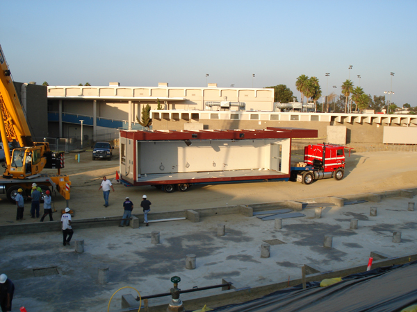 Crane setting a modular unit as the crew watches from the pad