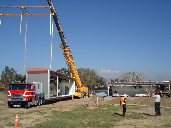 Crane and truck delivering a modular building section to the site