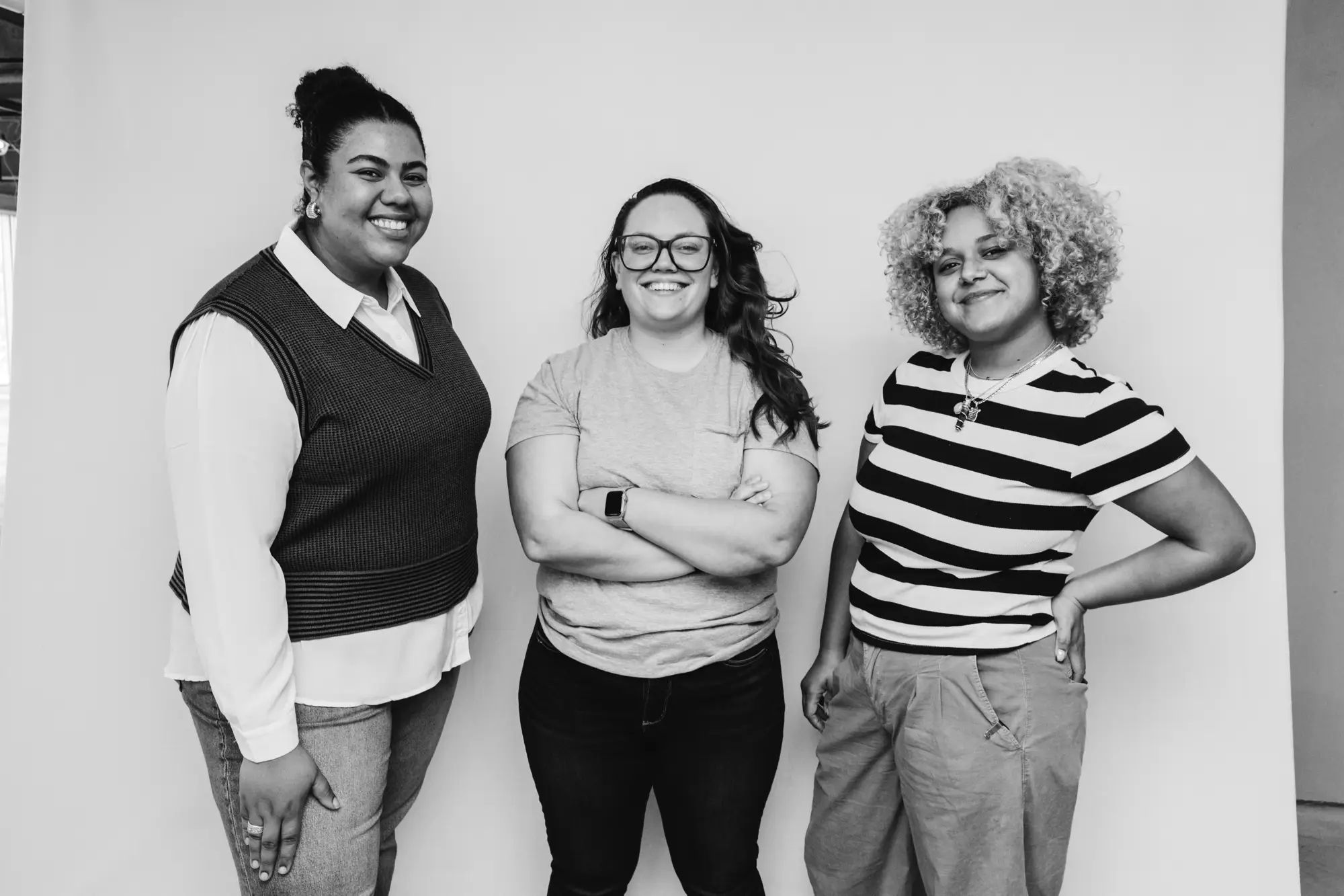 Three smiling women standing side by side against a plain background.