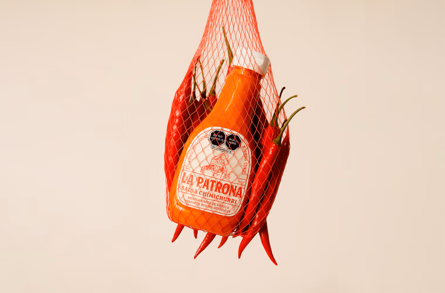Botella de salsa chimichurri La Patrona rodeada de chiles rojos dentro de una bolsa de malla roja.