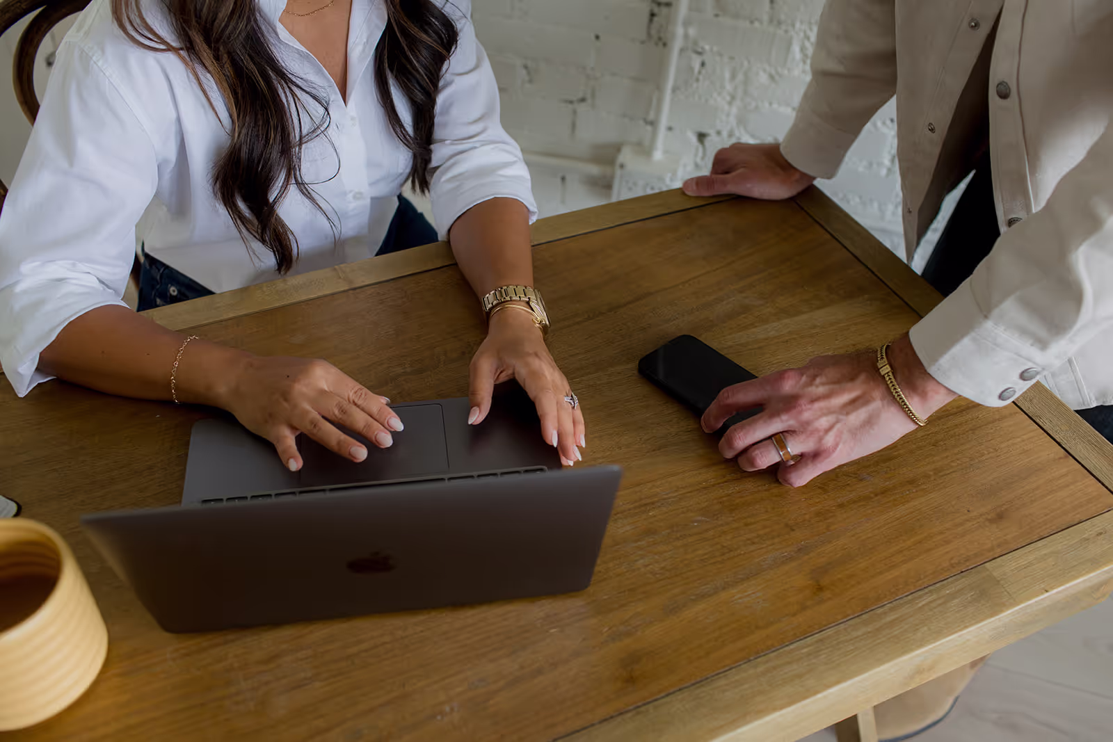 Two people collaborating at a laptop on a wooden table.