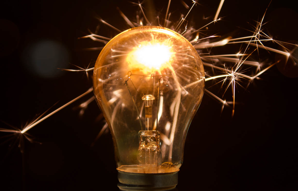 A lightbulb that is being illuminated by a sparkler. The sparkler is creating little explosions/fireworks around the small lighbulb