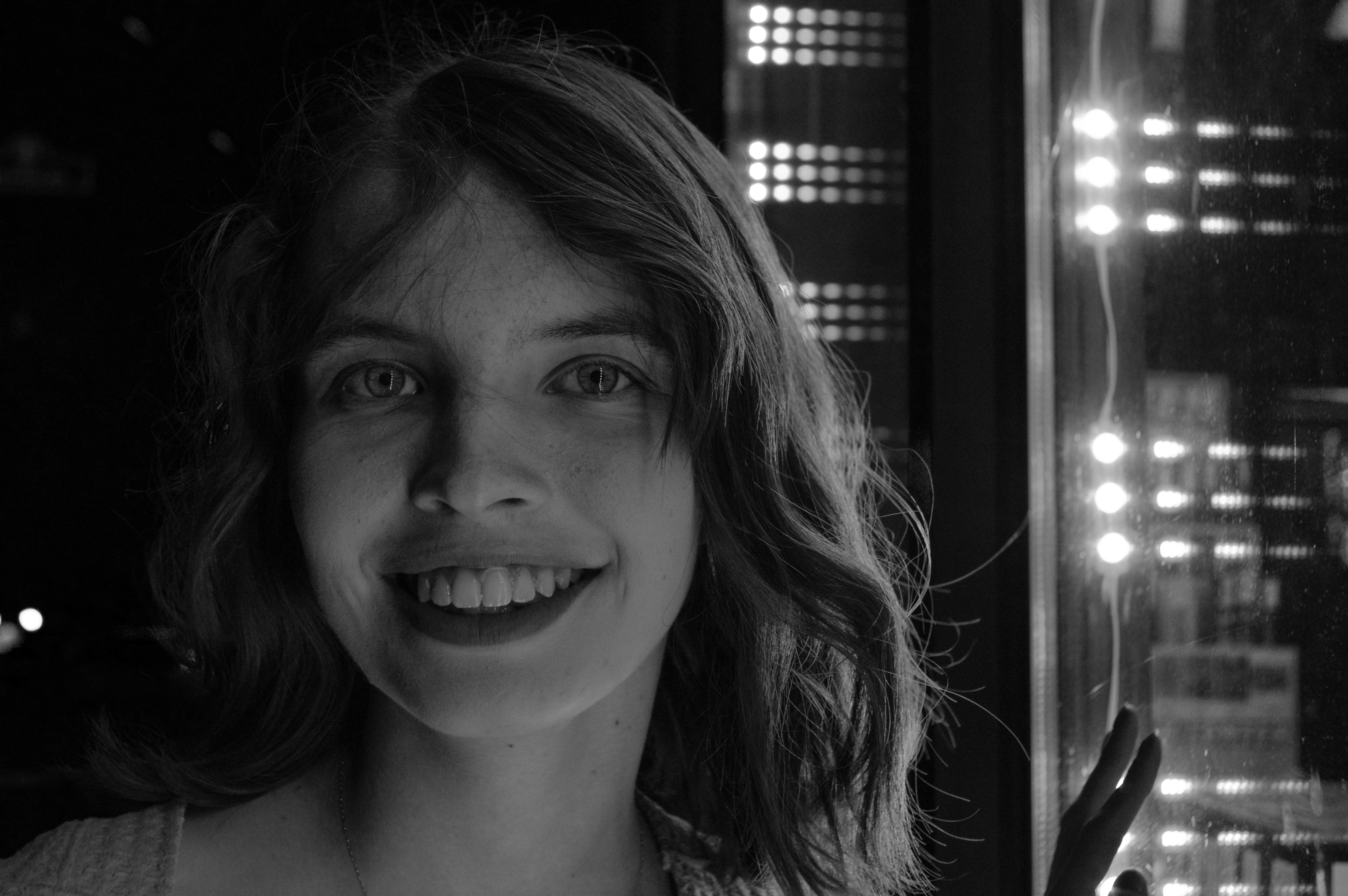 A woman photographed on the street in downtown Bloomington in 2022 with some of the colorful neon signage in the background. The photo is in black and white.