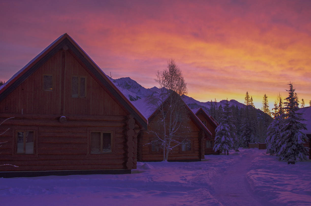 Sunrise in the Canadian Rockies in Banff, Alberta, Canada. The sunrise is beginning to appear in its vibrant pink, purple, and orange behind some small chalets in the wintery mountains of Canada.