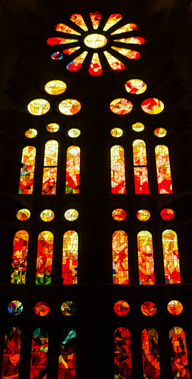 A stained glass window inside the famous Sagrada Família cathedral in Barcelona, Spain. This window is mainly red and orange with some yellow and some blue and green in the bottom left.