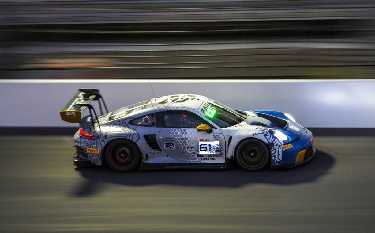 A high speed Porsche 911 GT car racing down the front straightaway at the Indianapolis Motor Speedway during the night of the 8 hour race in the summer of 2024. 