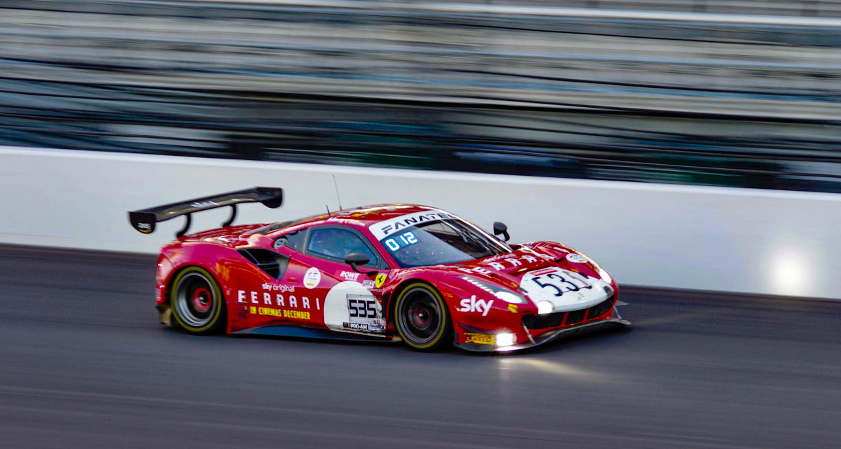 A red Ferrari 296 GT3 racing into the night at the 2023 IMSA 8 Hours at Indy during October.