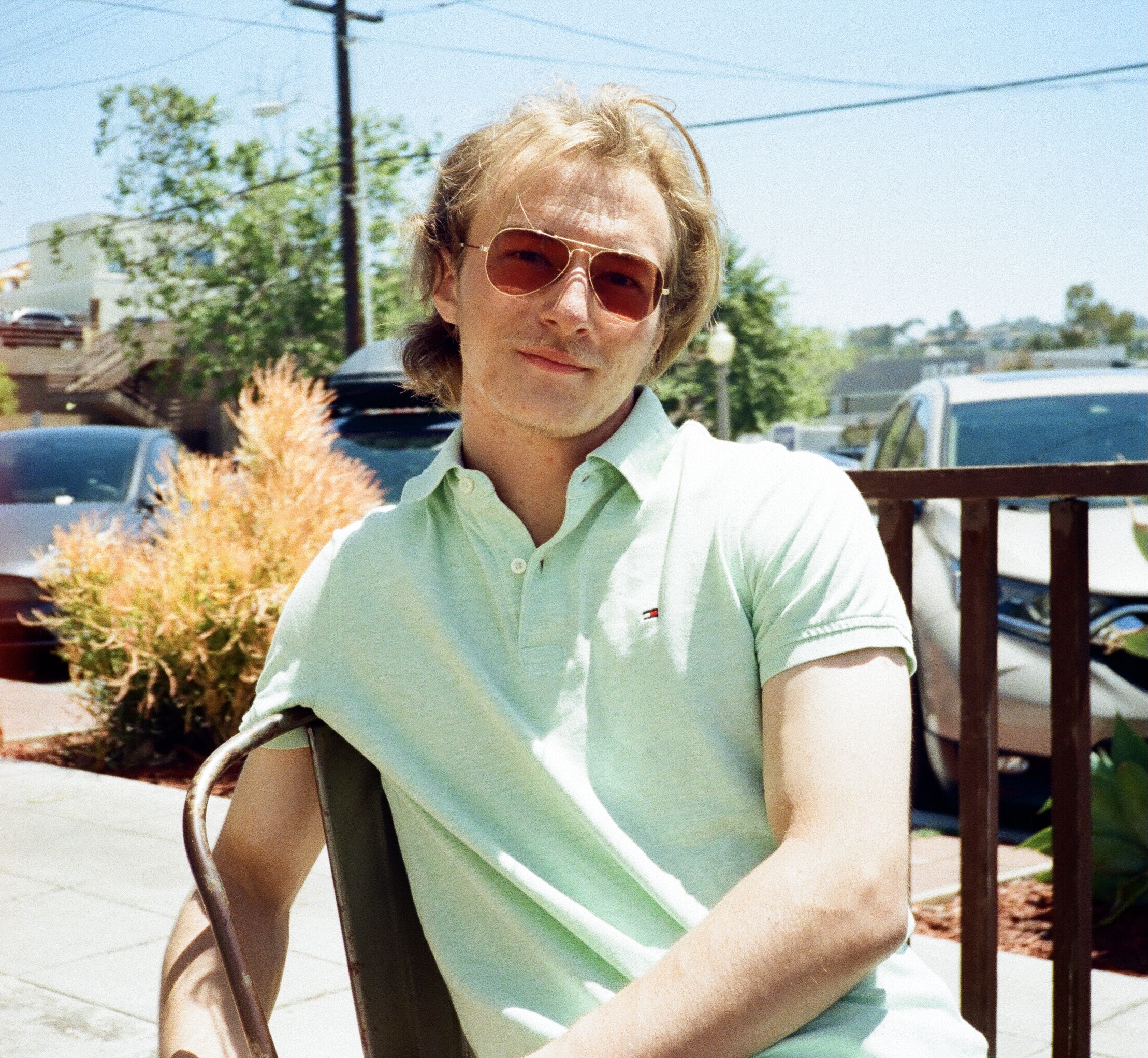 A good looking blonde haired man wearing a light green polo shirt and Ray-ban sun glasses in La Jolla, California. The man is looking at the camera.