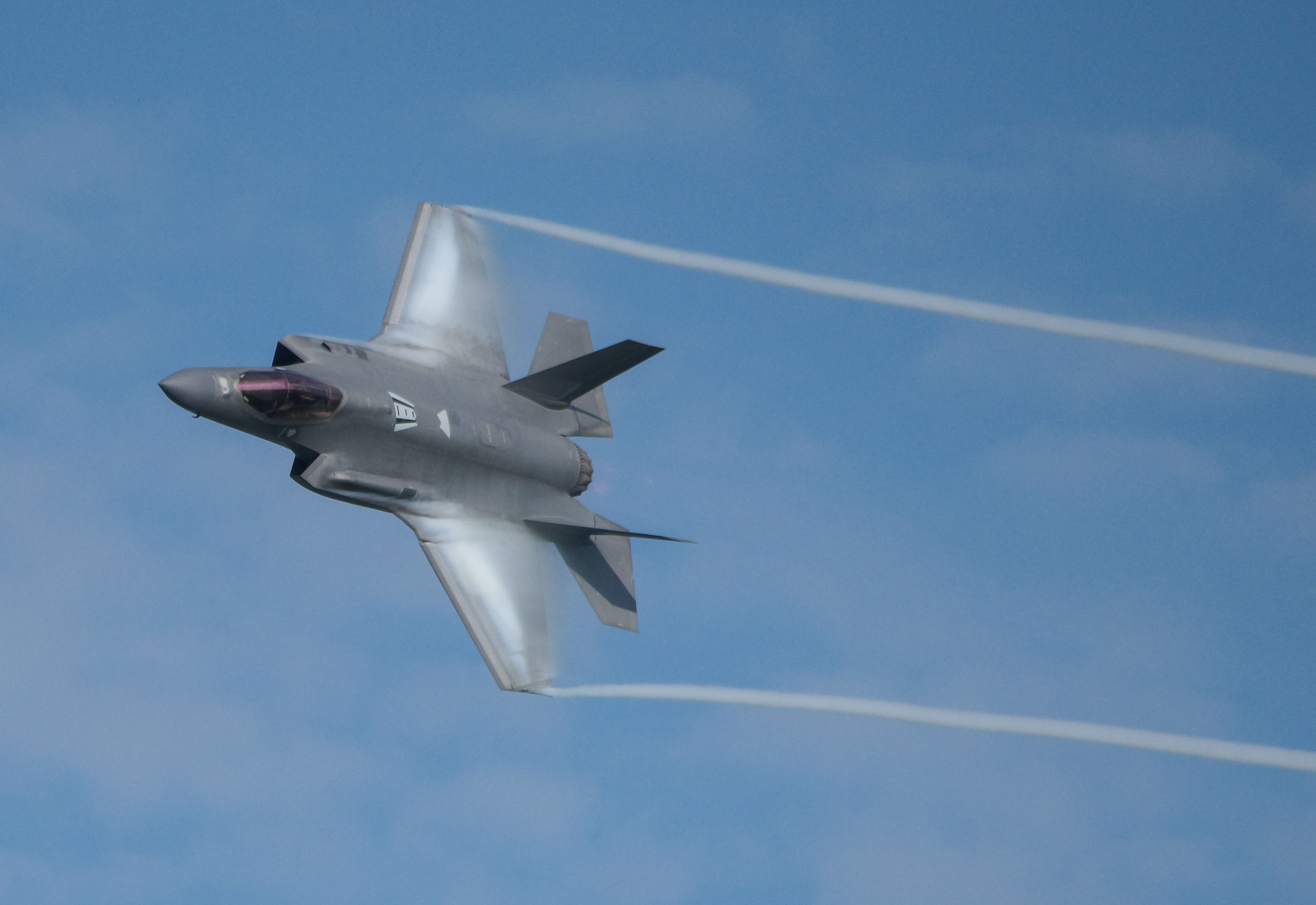 A green and white BMW M4 race car racing at high speeds down the front straight at the Indianapolis Motor Speedway during the 8 hour race. The image shows the car's headlights and number on the side of the car are illuminated which means that the photo is taken during dusk.