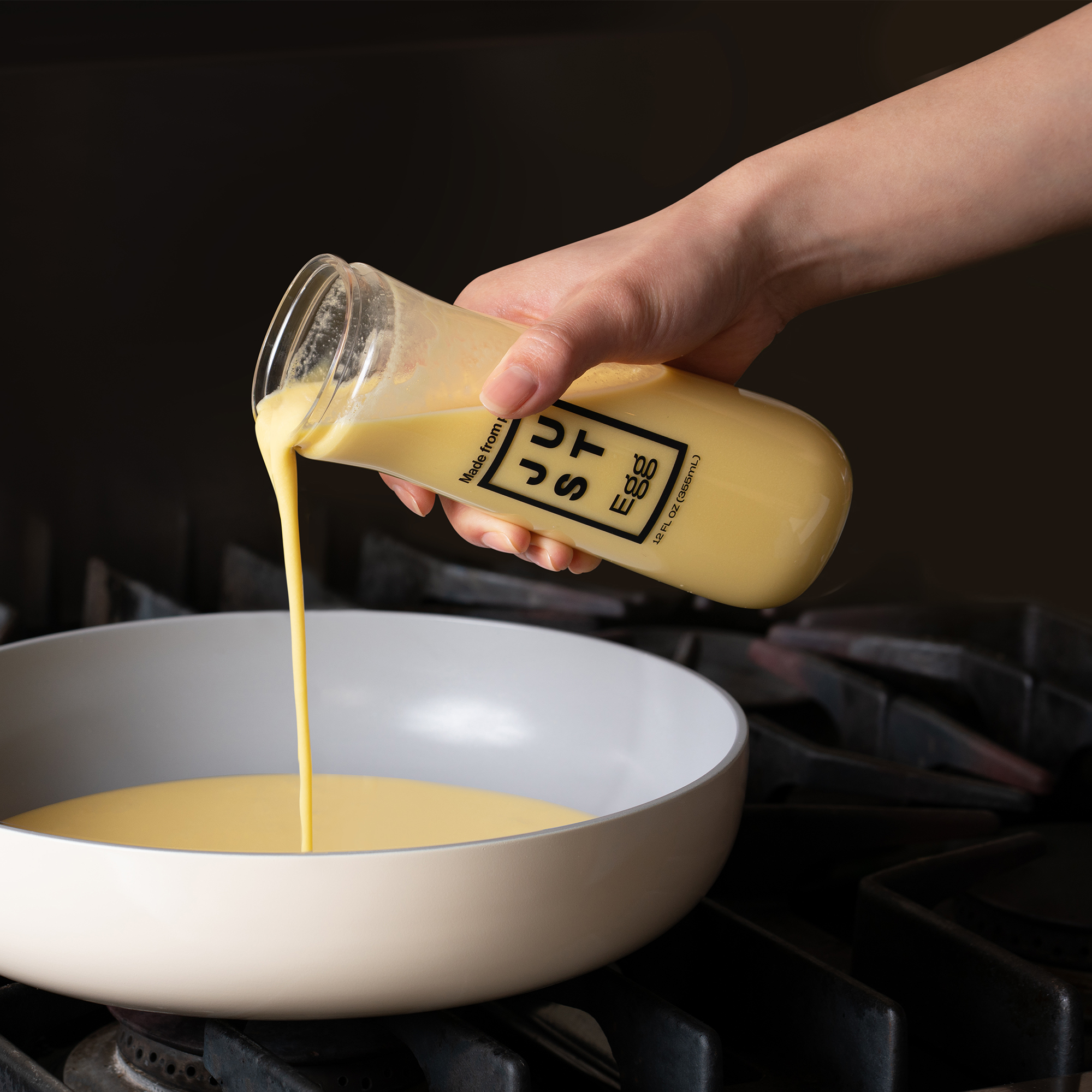 A hand pouring Just Egg from the glass bottle design on to a pan.
