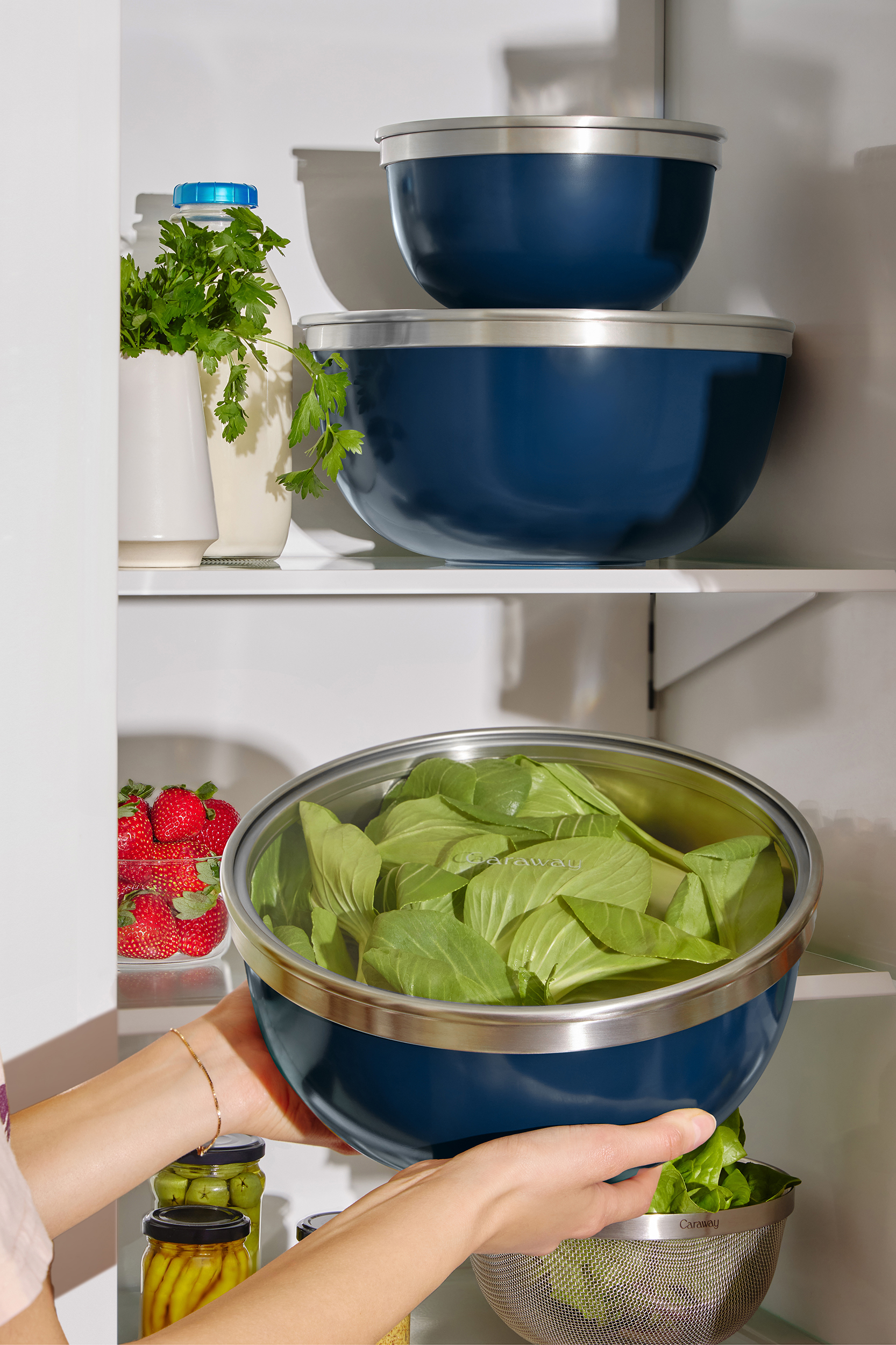 A person putting a Caraway Mixing Bowl in a fridge.