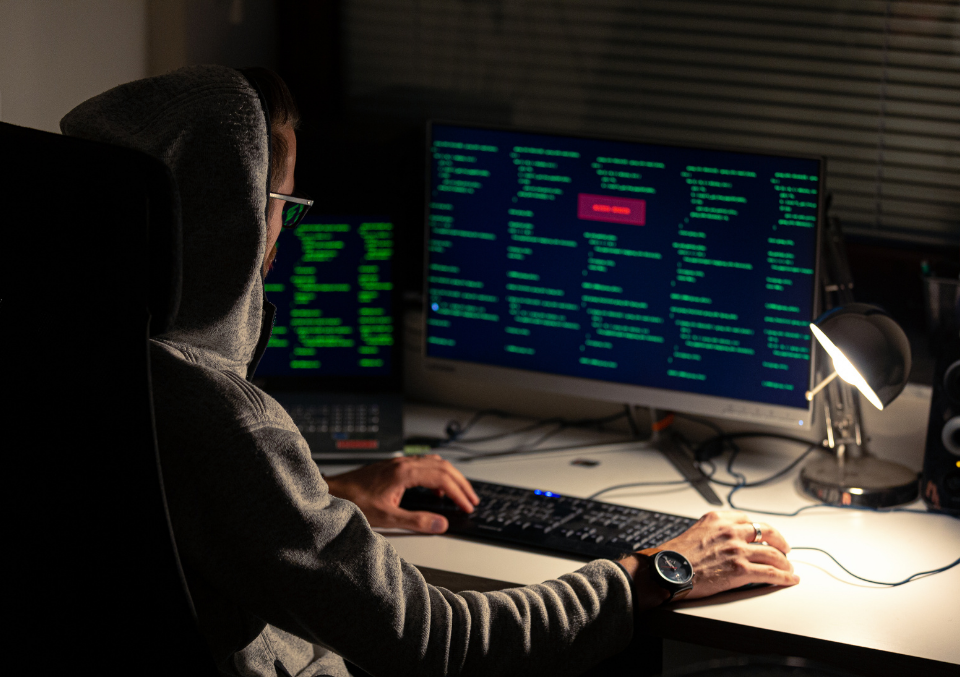 A developer or cybersecurity professional working late in a dim office environment, focusing on code displayed on a dual-monitor setup.