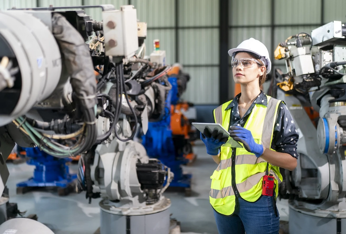 A woman in a yellow safety vest is standing in front of a machine.