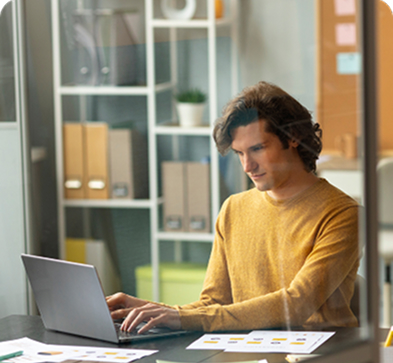 A person working diligently on a laptop referring to various documents