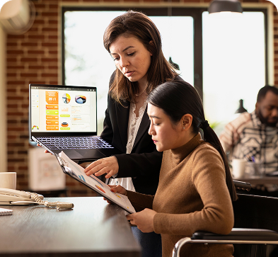 An expert with a laptop checking the work done by a subordinate by referring to a document