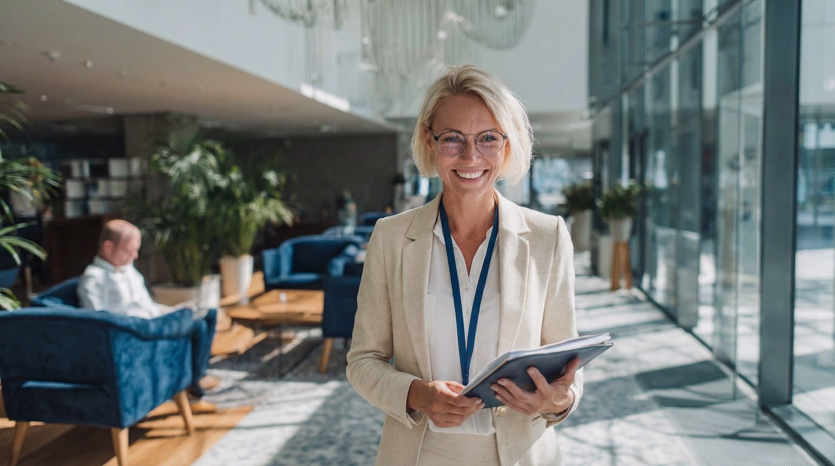 Lächelnde blonde Frau mit Brille und Akten im modernen Büro mit Glasfassade.