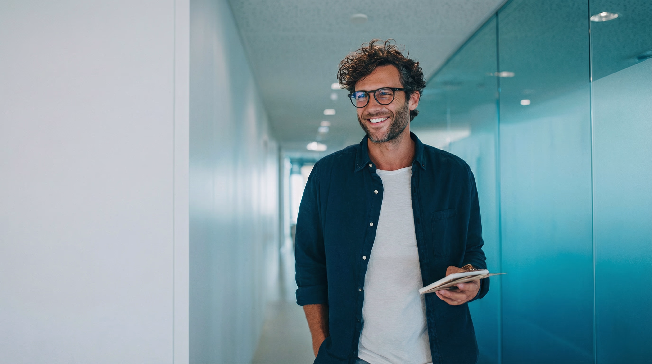 Lächelnder Mann mit Brille hält Klemmbrett in modernem Büroflur.