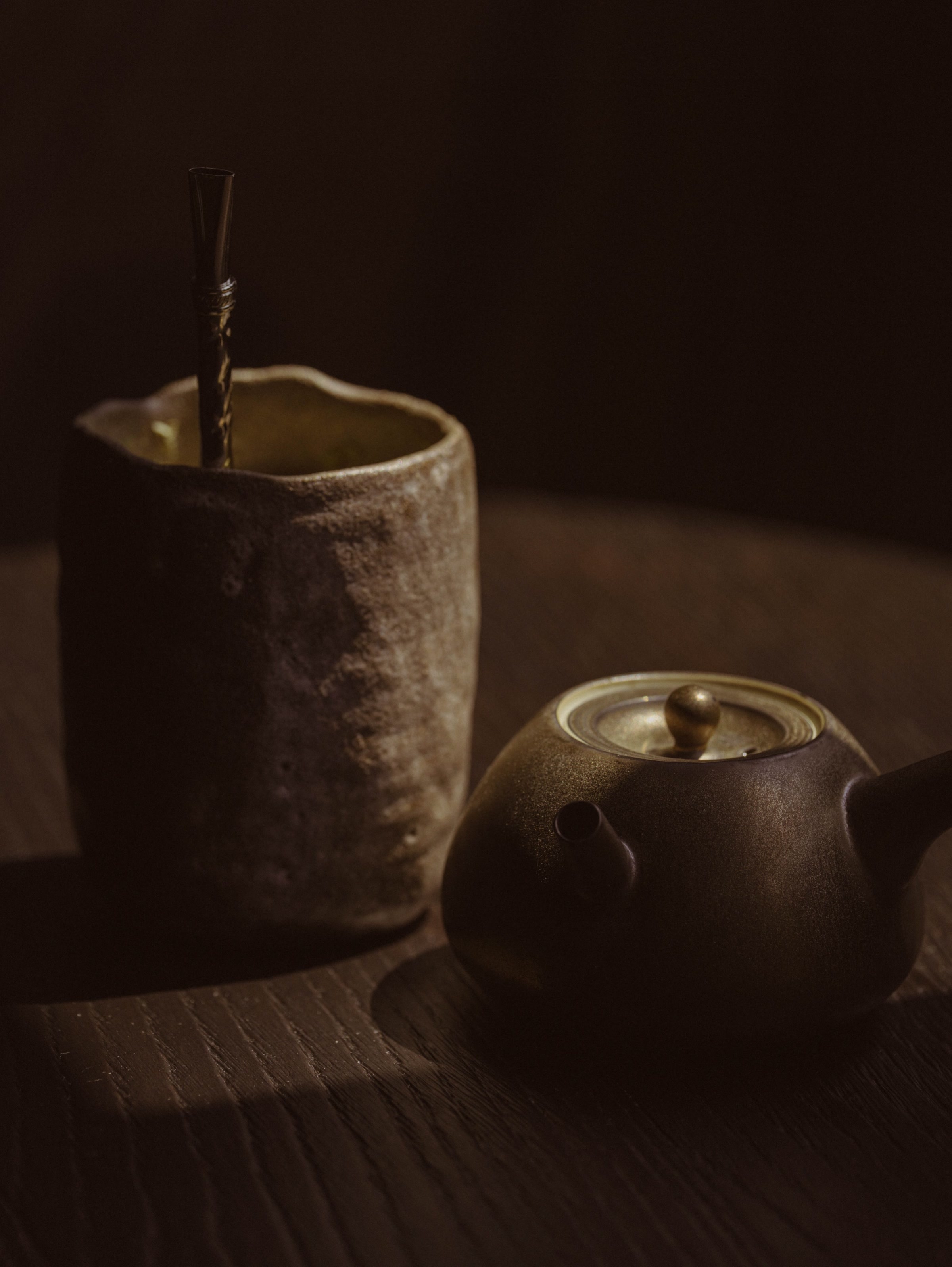 Textured ceramic cup with bombilla and dark teapot on wood at SUR Milano