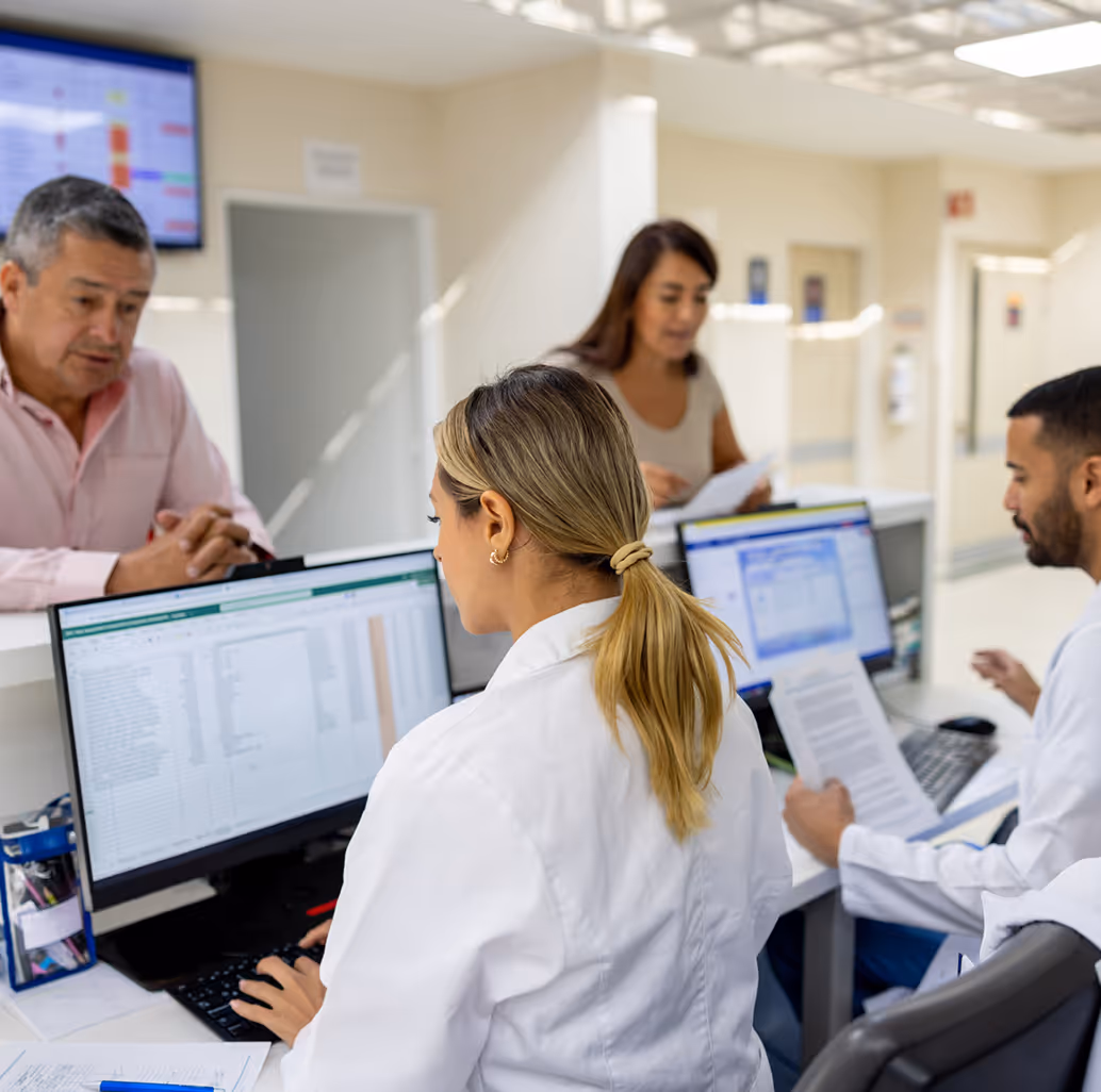 Medical staff working at a hospital front desk with computers, assisting patients in a bright, modern setting.