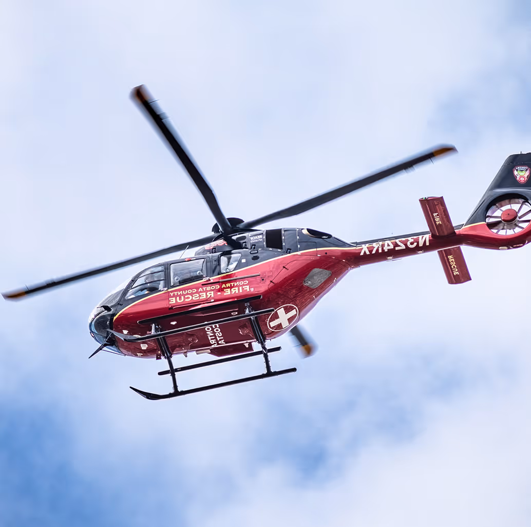Red and black emergency medical helicopter in flight against a cloudy sky.