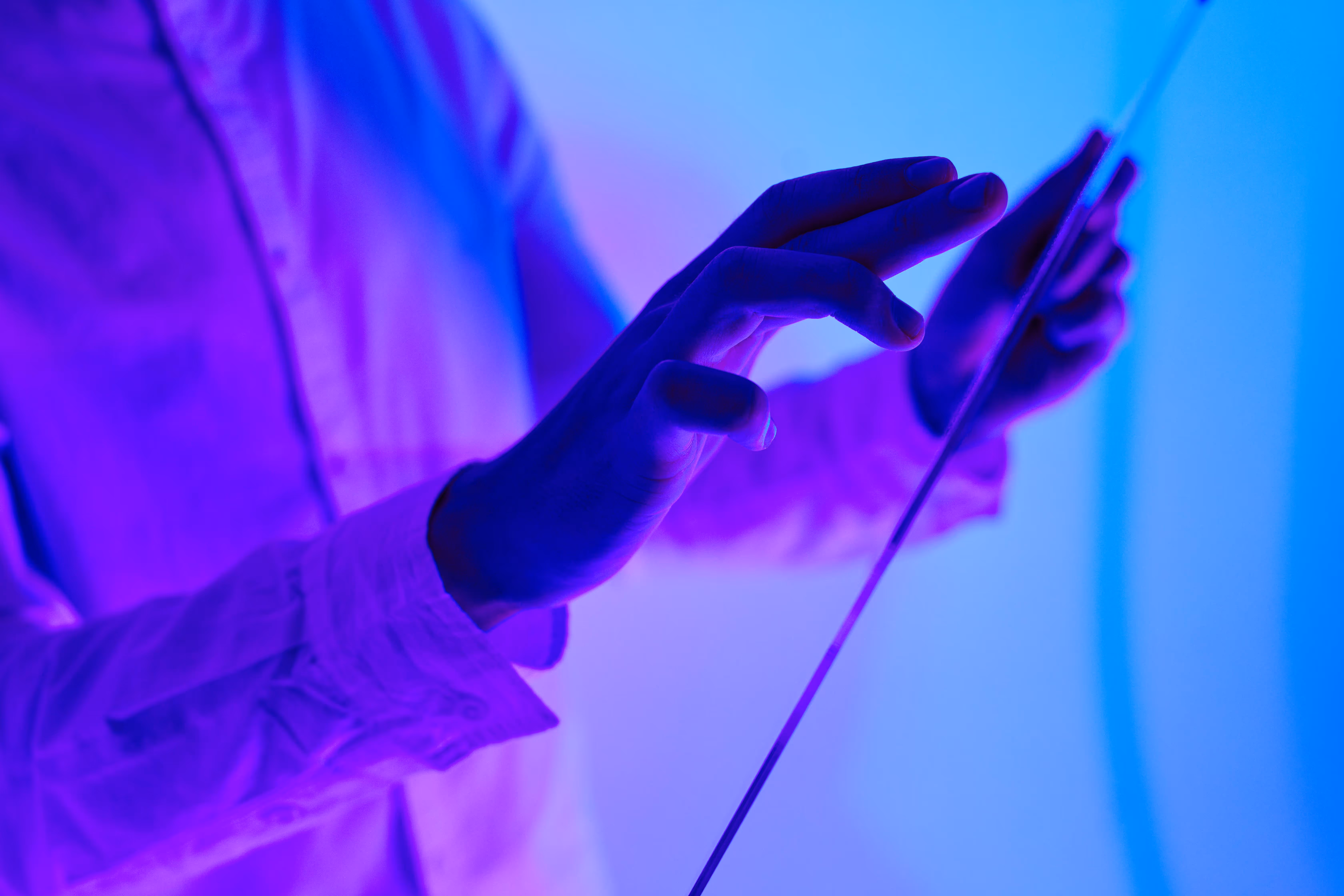Close-up of two hands holding glowing motion controller devices in a dark room with blue and purple lighting.