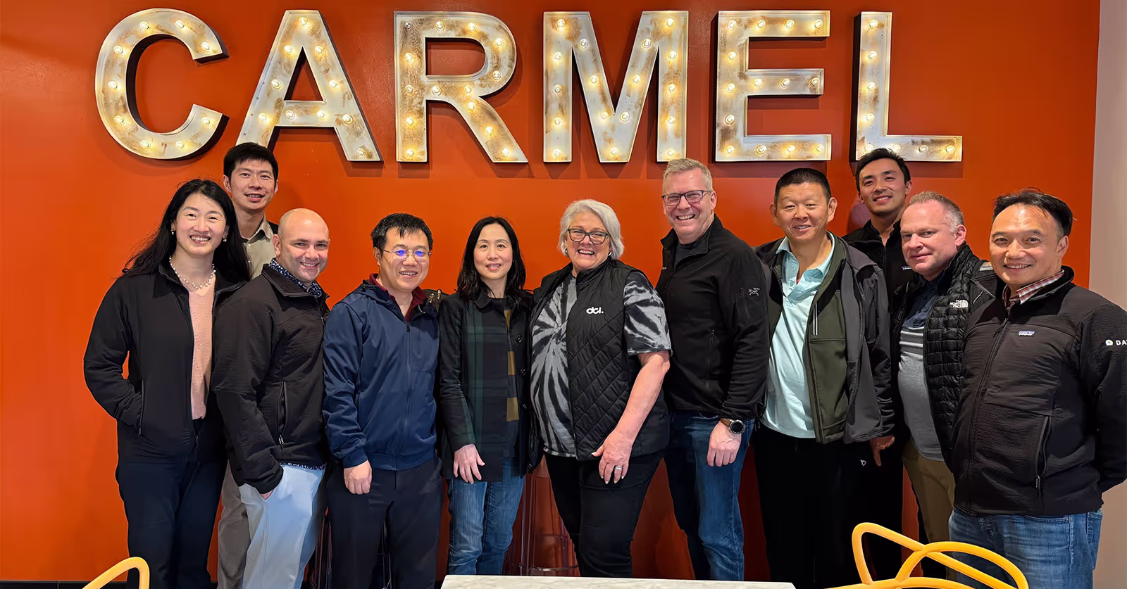 A group photo with red background and CARMEL logo in behind