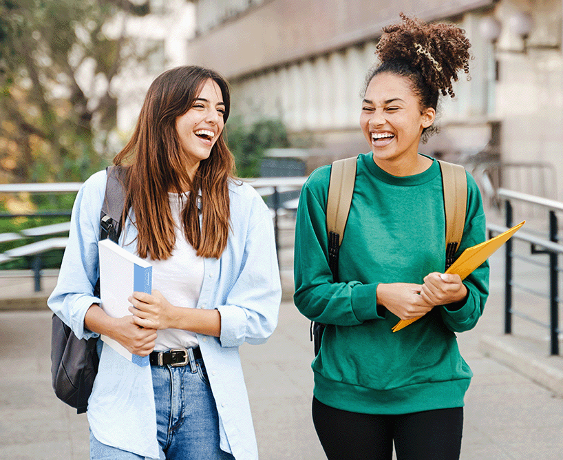 Zwei Studentinnen lachen und unterhalten sich auf dem Campus – das Bild steht sinnbildlich für die positiven Erfahrungen im Studium und beantwortet visuell die Frage: Was ist ein duales Studium?