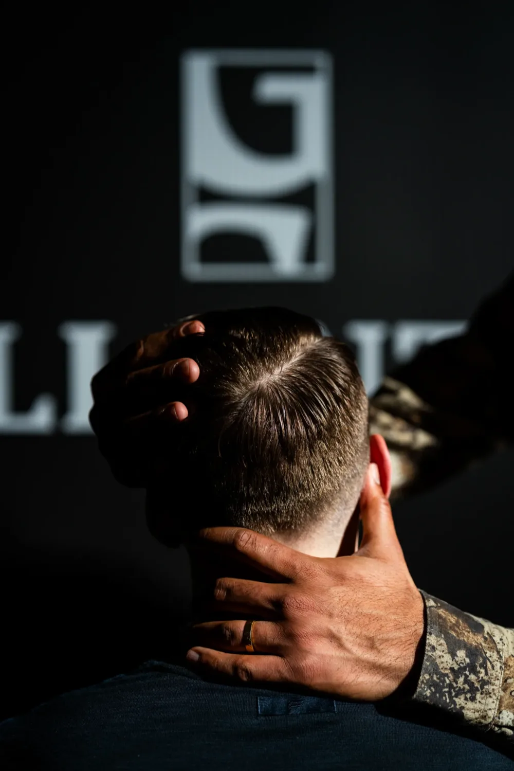 A barber shaping a client's hair beneath the Gallantier crest