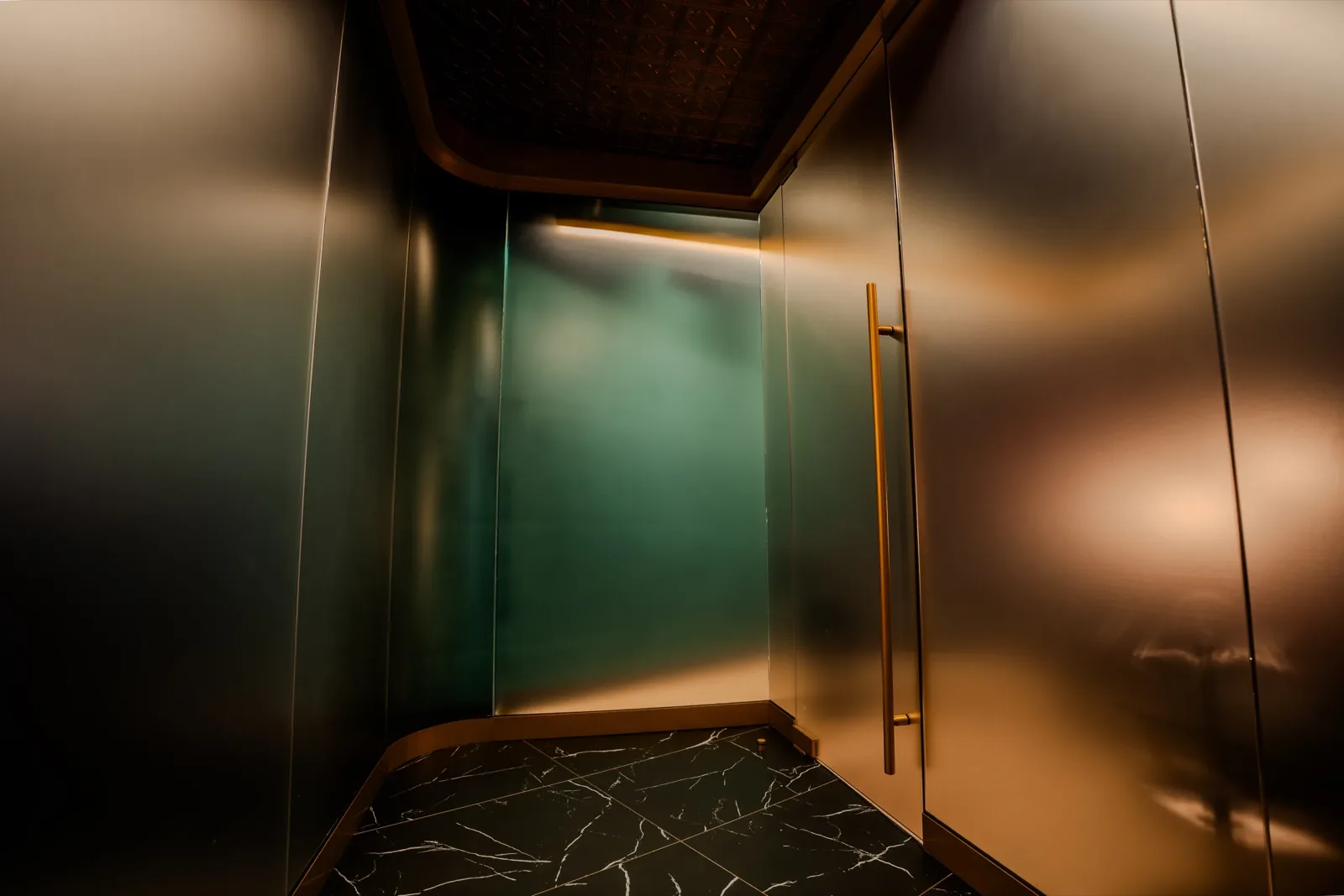 A brass door handle against the green glass wall