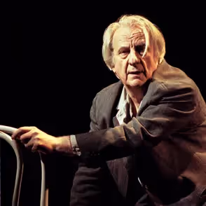 Elder performer on stage at Festival di Spoleto, leaning on chair dramatically