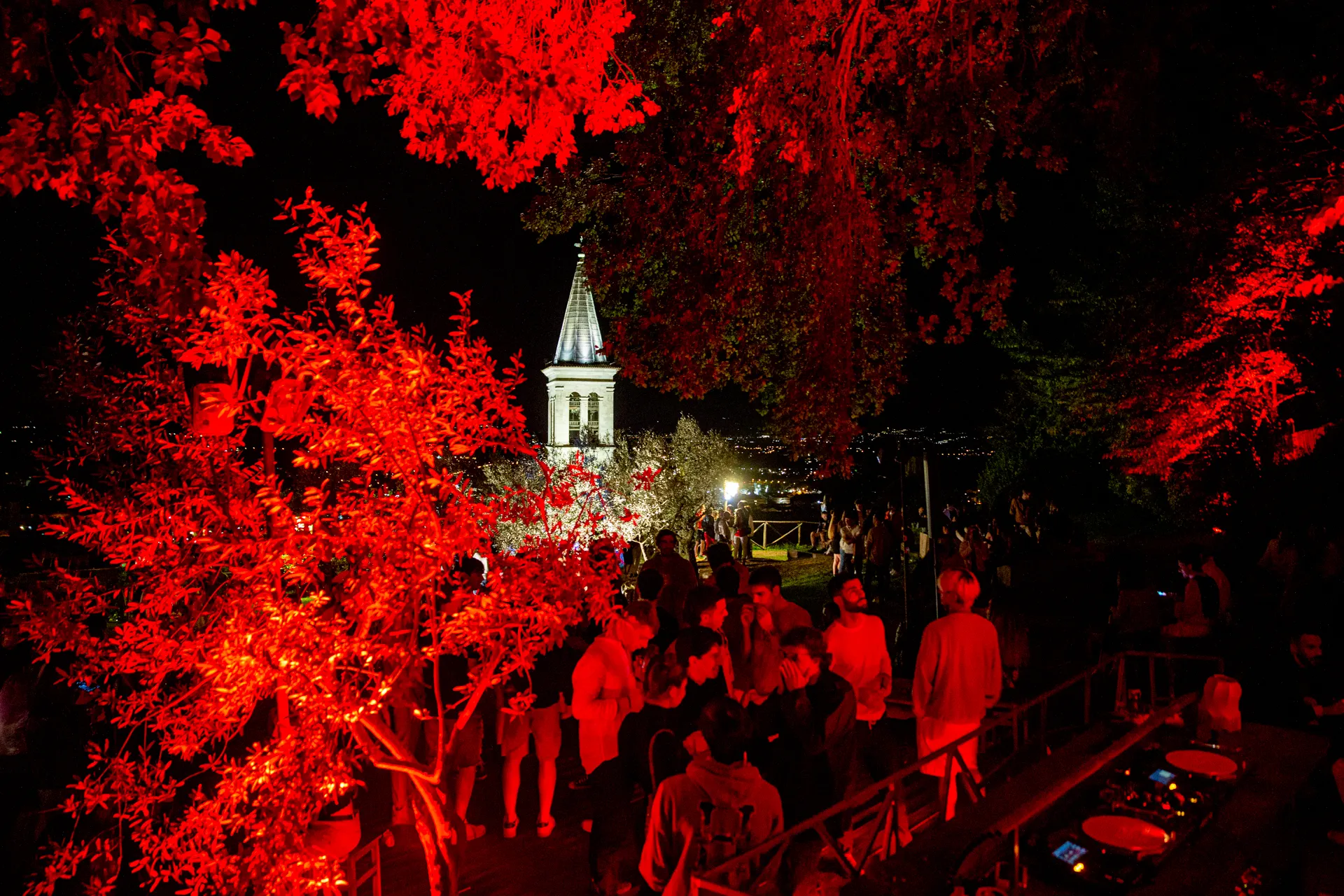 Atmosfera notturna al Festival di Spoleto con alberi rossi e campanile illuminato