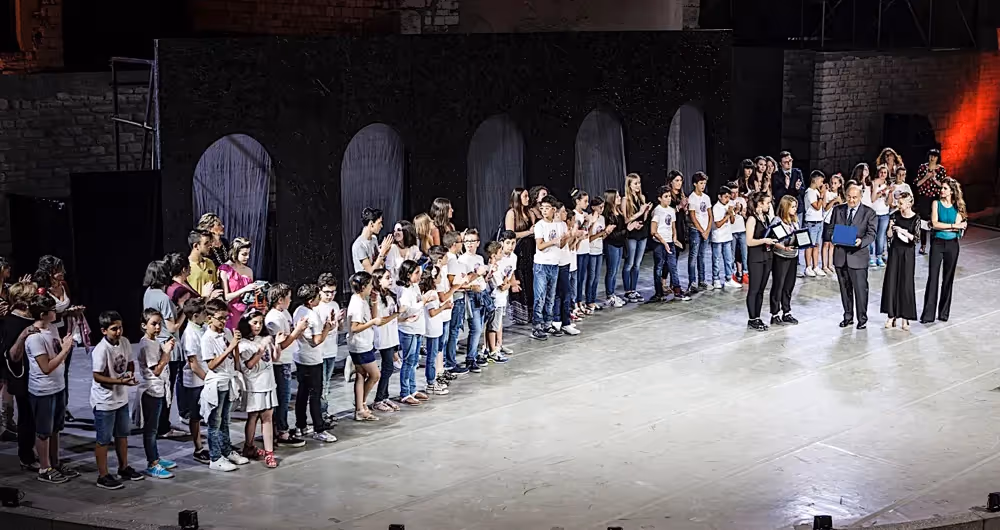 Giovani performers al Festival di Spoleto, schierati sul palcoscenico in bianco e nero