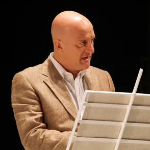 Artista calvo sul palco durante il Festival di Spoleto, concentrato su un laptop