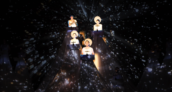 Festival di Spoleto performance featuring illuminated figures against starry cosmic backdrop